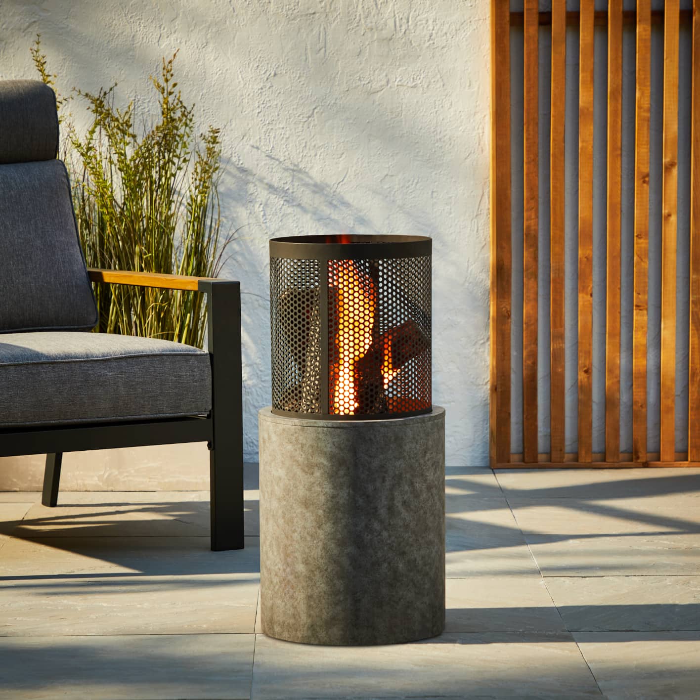 A lit For Living Wood Burning Fire Column on a patio with outdoor furniture. 
