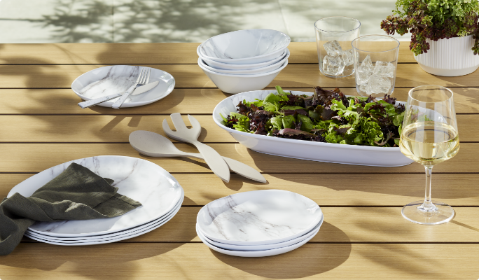 A variety of CANVAS Faux Marble Serveware on a table with a salad and serving utensils.