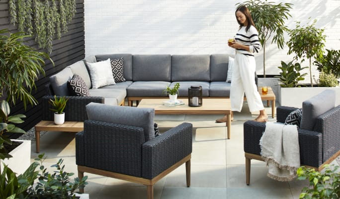 A woman admiring her CANVAS Edenvale sofa, coffee table and armchairs on a patio.