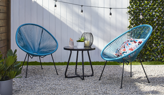 Two CANVAS Acapulco Collection chairs and a side table in a backyard.