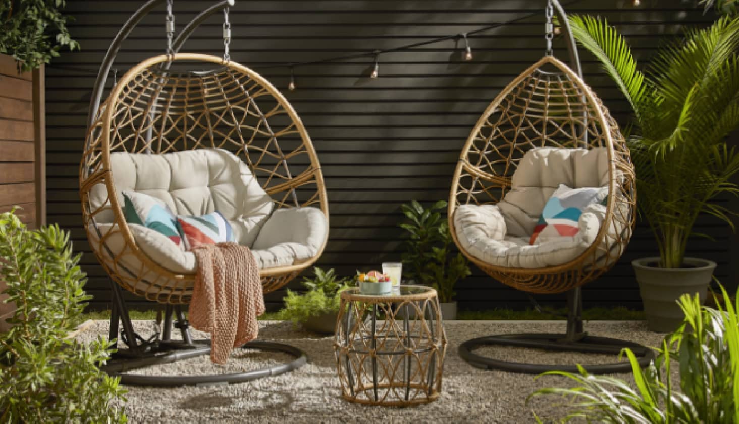 Deux fauteuils ovoïdes CANVAS Sydney dans un jardin avec une table d’appoint. 