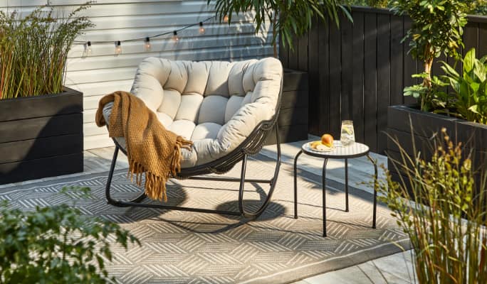 A CANVAS Cove Rocking Chair and a side table in a backyard. 
