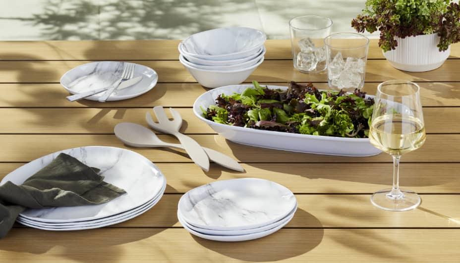 Une gamme de plats de service en faux marbre CANVAS sur une table avec de la salade et du vin. 