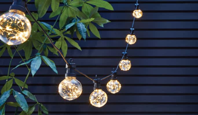 A glowing string of CANVAS Enchant Fairy Orb lights hanging on a patio.
