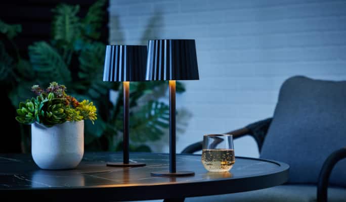 Two CANVAS Raven Table Lamps on a patio table at night.