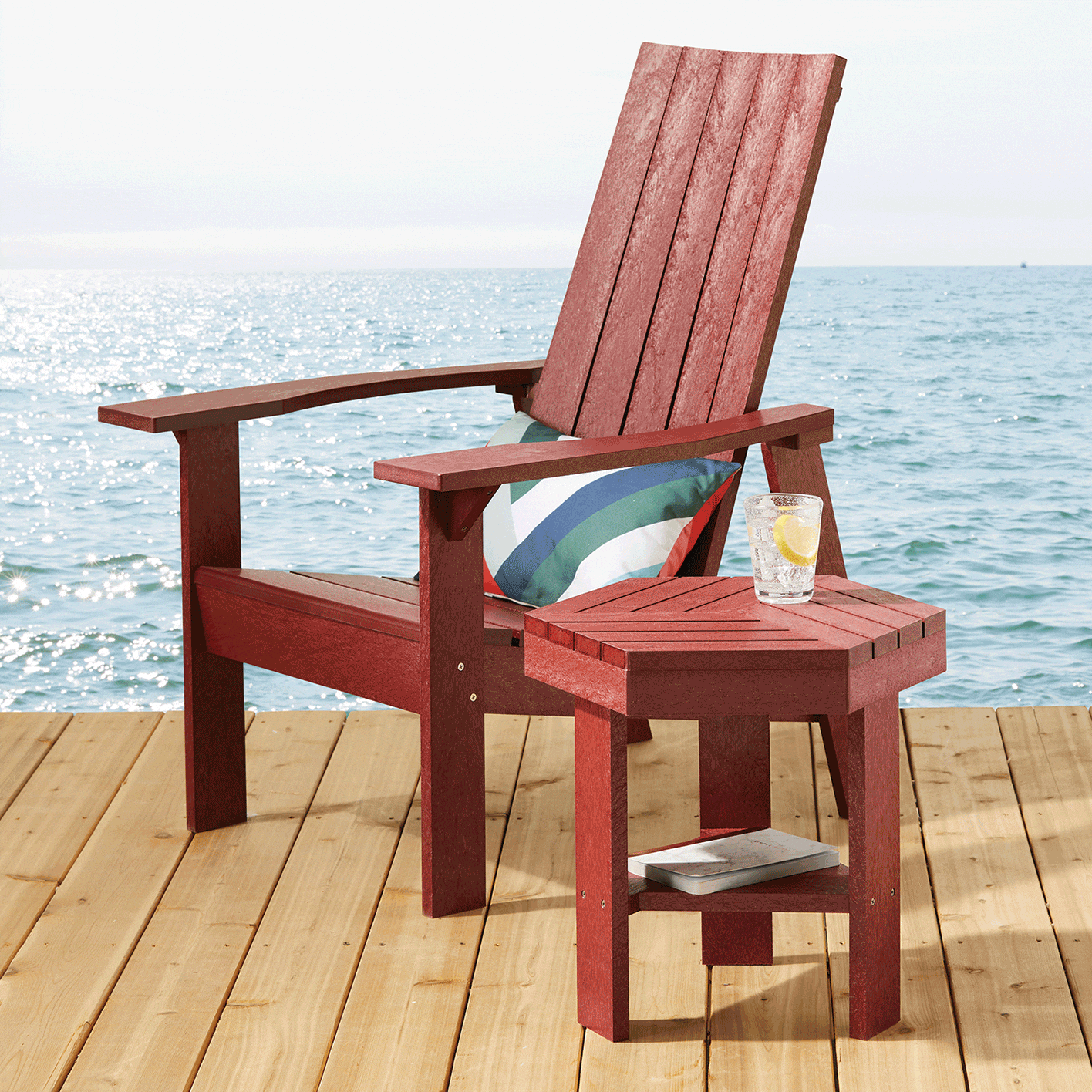 A red CANVAS Arrowhead Muskoka Chair and side table on a lakeside dock. 