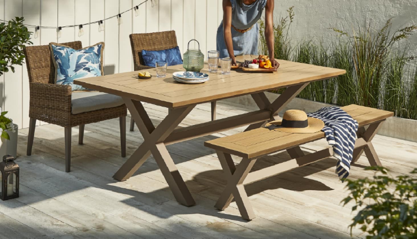 A woman putting a tray of food on a CANVAS Belwood Dining set in a backyard. 