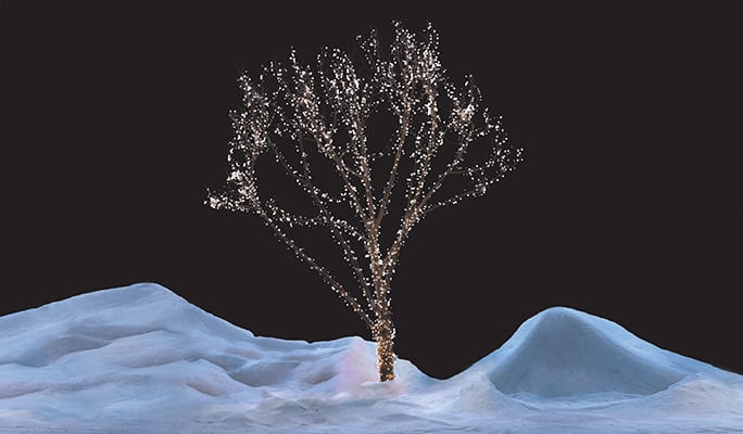 A tree covered with glowing, white Christmas lights and surrounded by snow.
