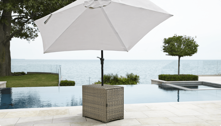 Une table pour parasol CANVAS Bala installée sur une terrasse au bord de la piscine avec un parasol gris.