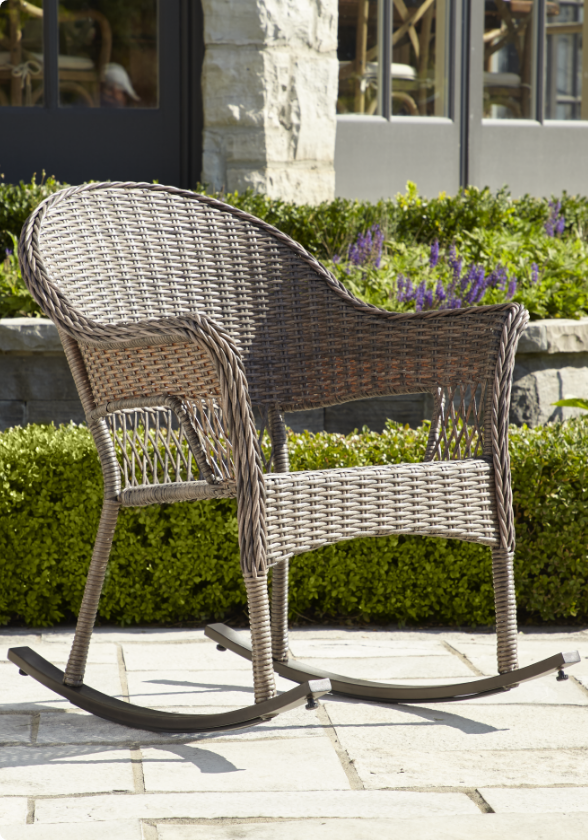 Un fauteuil berçant en osier CANVAS Canterbury sur un patio.  