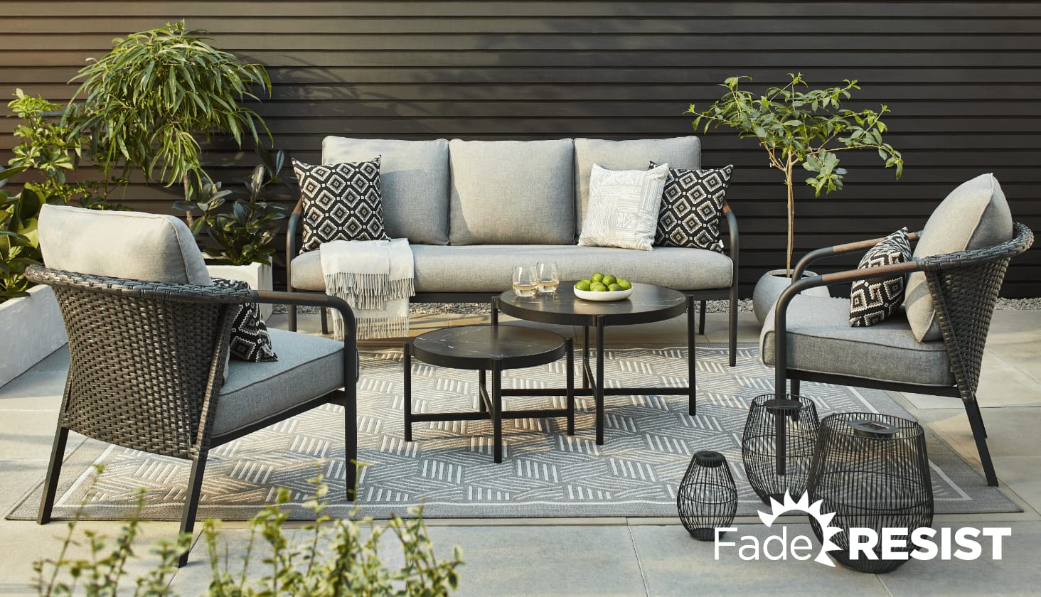 Sofa, fauteuils et tables gigognes CANVAS Jasper sur un patio avec des plantes, un tapis extérieur et des lanternes. 