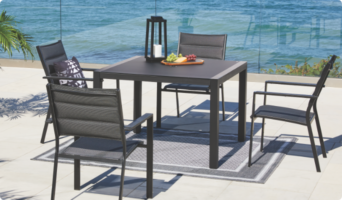 Une table carrée CANVAS Mercier et des chaises sur une terrasse au bord de l’eau.