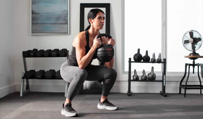 A woman squatting with a Weider Rapid Strike 30lb adjustable kettlebell.