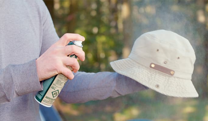 An adult spraying a bucket hat with bug repellent. 