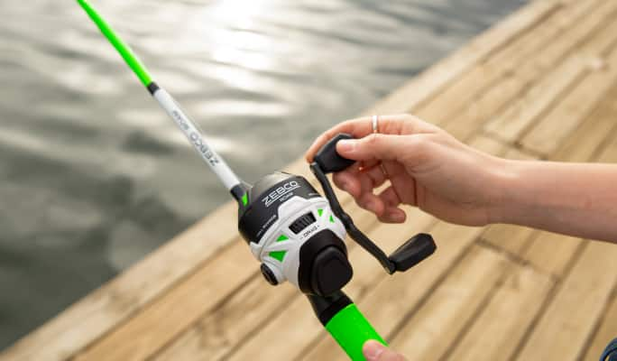 An adult turning the reel of a Zebco fishing rod. 