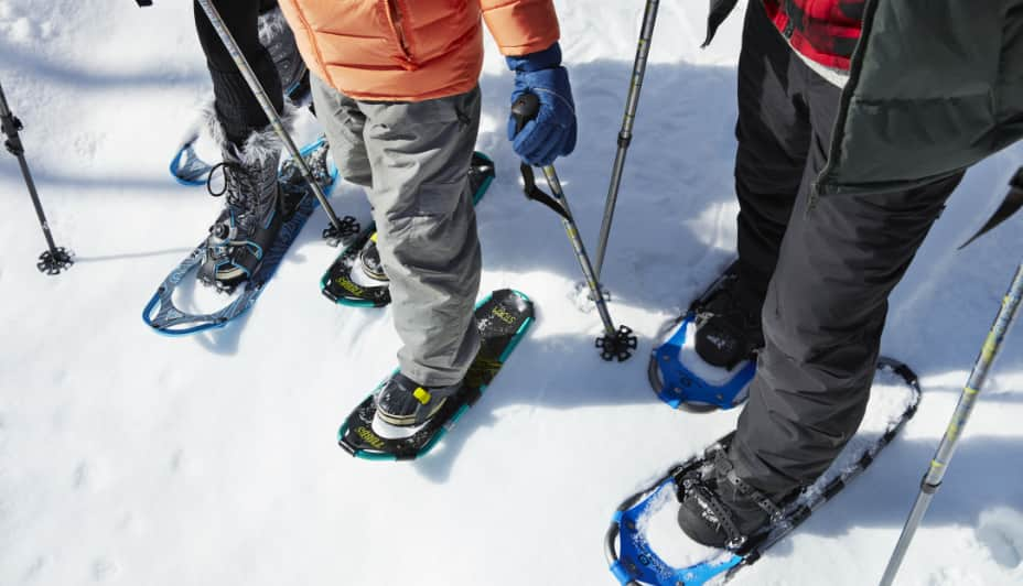 Deux adultes et un enfant pratiquant de la raquette à neige avec des bâtons de randonnée.