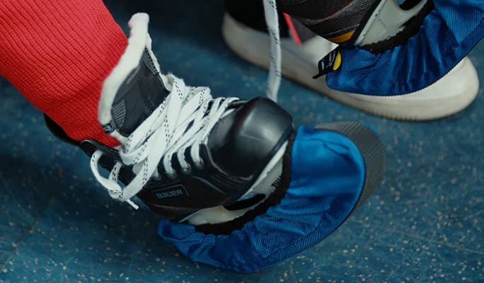 A child’s feet wearing untied hockey skates with blade guards. 