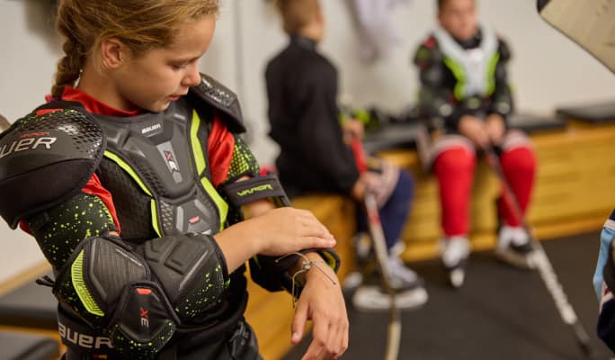 A girl fastening a wrist strap of hockey padding she is wearing. 