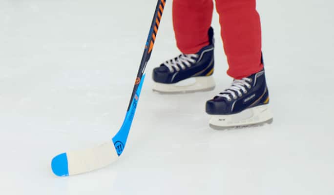 A player holding a bright blue, taped hockey on the ice. 