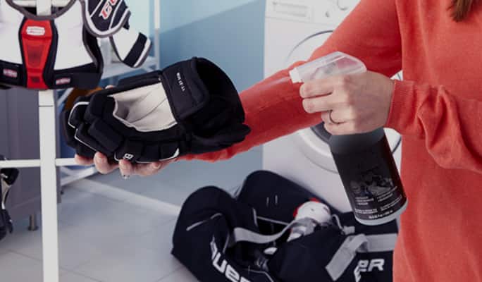 An adult spraying a cleaning solution onto a hockey glove. 