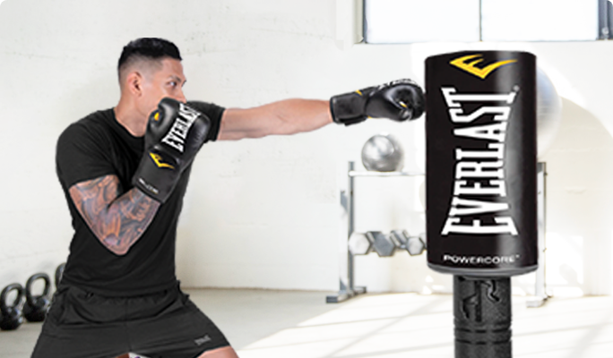 A man wearing boxing gloves, hitting an Everlast freestanding punching bag.