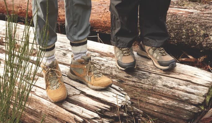 Two people standing on log wearing hiking boots
