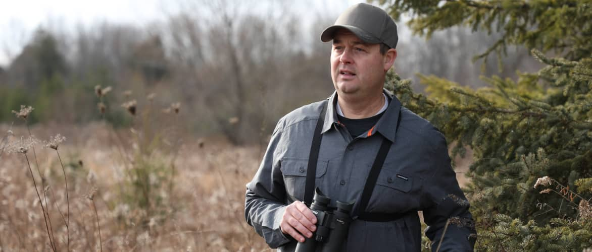 Person standing in woods holding binoculars