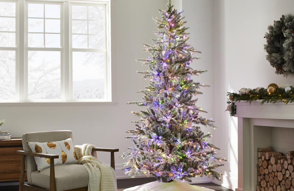 A flocked Christmas tree with multi-coloured lights in a living room. 