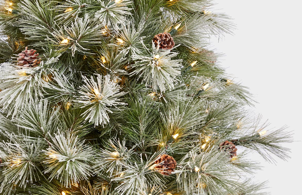 A section of branches on an artificial flocked, pre-lit Christmas tree with pinecones.  