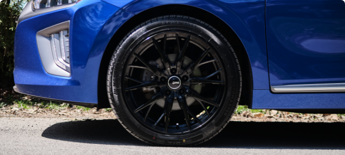 A  MotoMaster Hydra Edge tire on a blue car in an outdoor setting. 