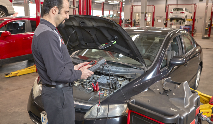 A technician inspects the battery of a car in a service bay.
