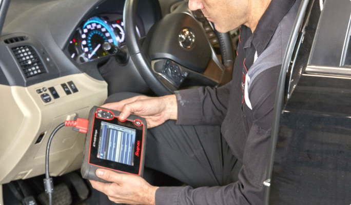 A technician uses a diagnostic tool to check a car’s systems.
