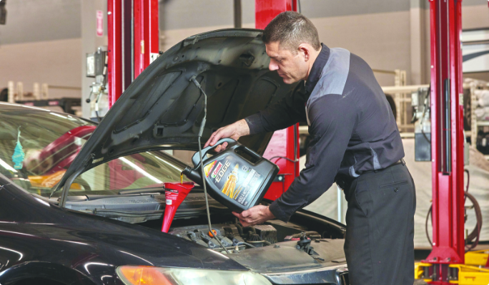 A technician uses a funnel to pour motor oil into a car’s oil reservoir.