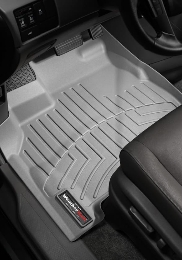 A light grey WeatherTech floor mat lines the driver’s-side footwell of a car with a black interior.