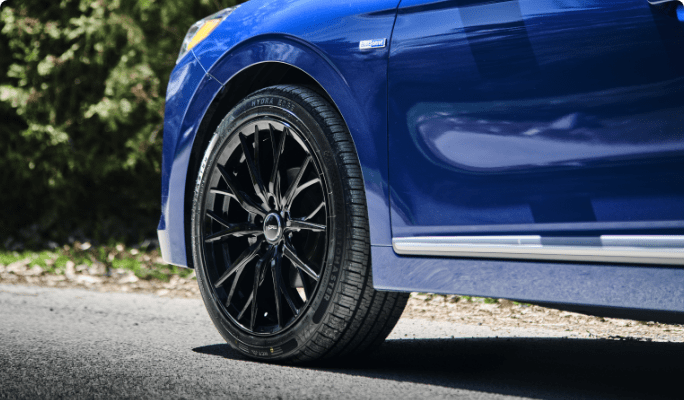 The front driver’s-side wheel of a blue car. 