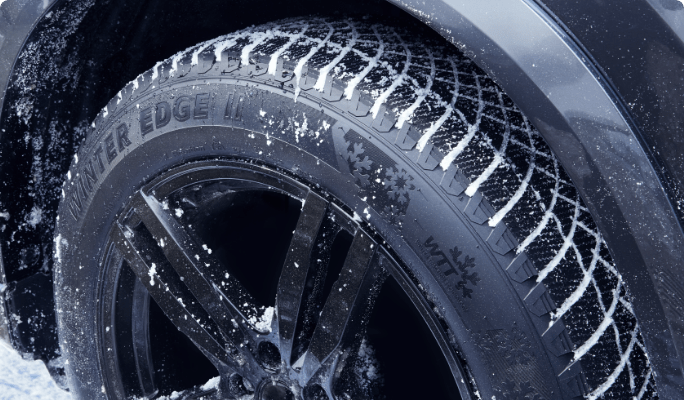 A MotoMaster Winter Edge II tire driving on a snowy road. 