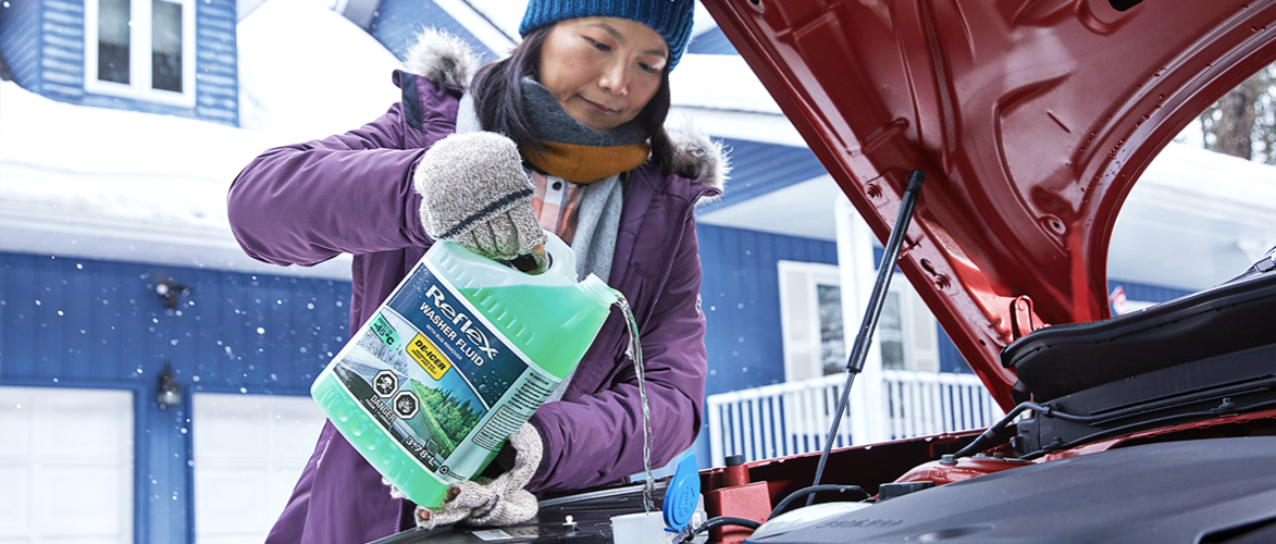 A motorist adds Rain-X washer fluid to a car’s reservoir.