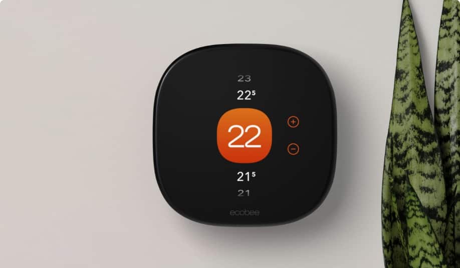A white smart thermostat reading “21°C” mounted on a beige wall near a sunlit living room.