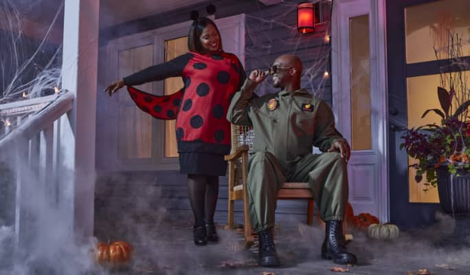 Two people wear Halloween costumes on a home's front porch.