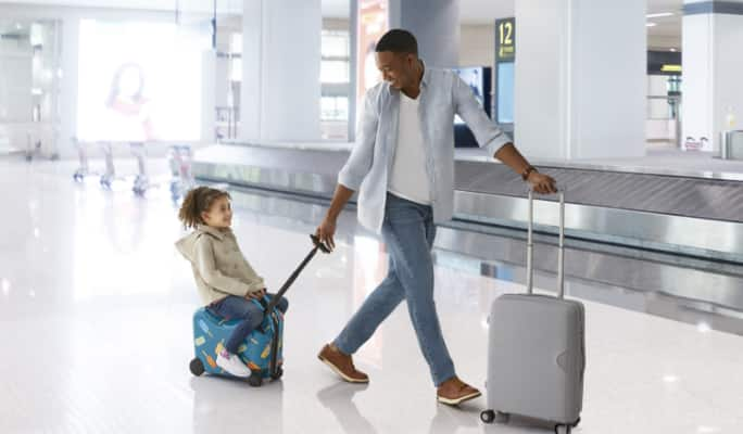 Un parent et son enfant transportent leurs bagages dans un aéroport.