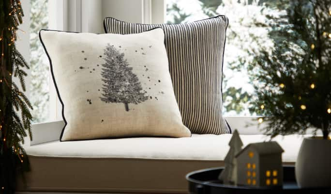 Christmas cushions, decorations and a mini tree near a window seat.