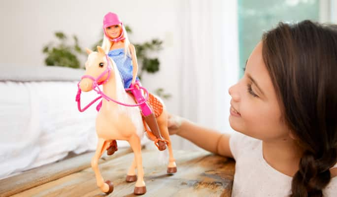 A girl playing with Barbie and horse toys. 