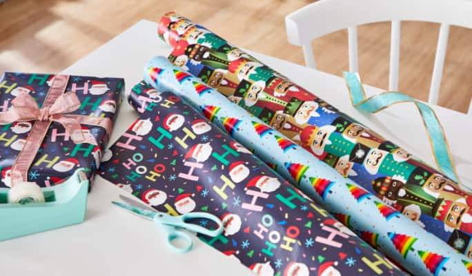 Rolls of CANVAS Merry Mingle wrapping paper in a table.