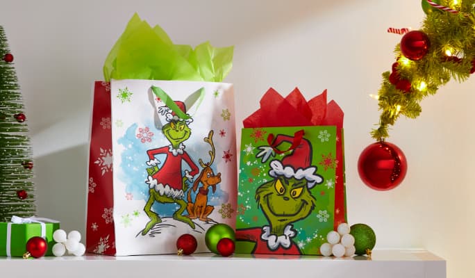 Two Christmas gifts in Grinch gift bags on a shelf. 