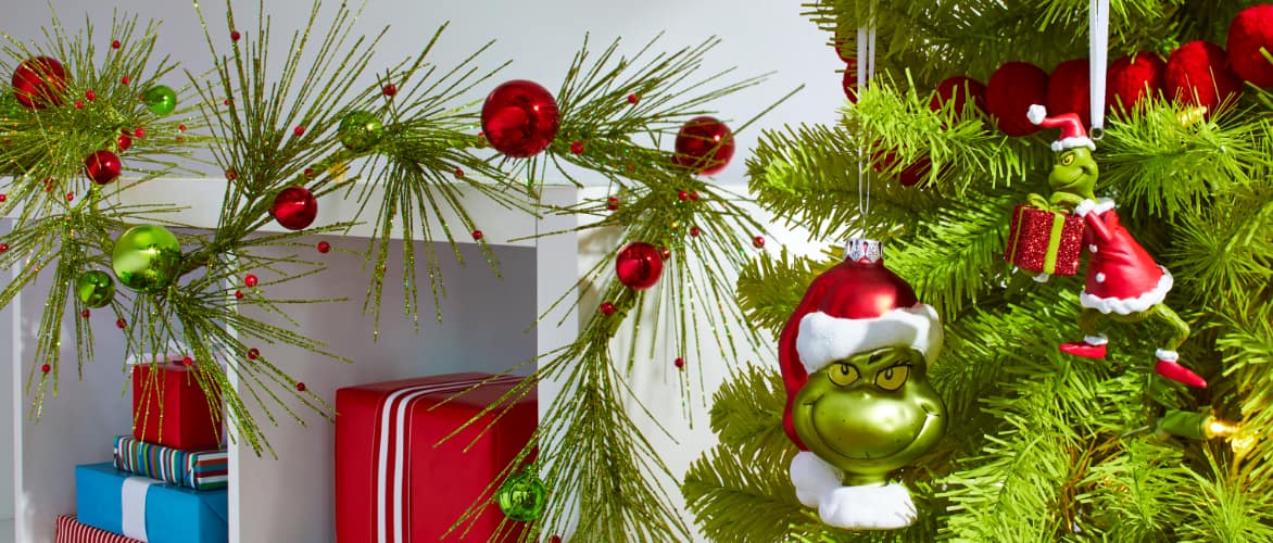 A tree decorated with Grinch ornaments and a shelf with Green Glitter Red Ball Garland.