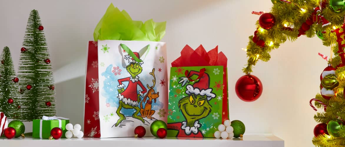 Two Christmas gifts in Grinch gift bags on a shelf. 