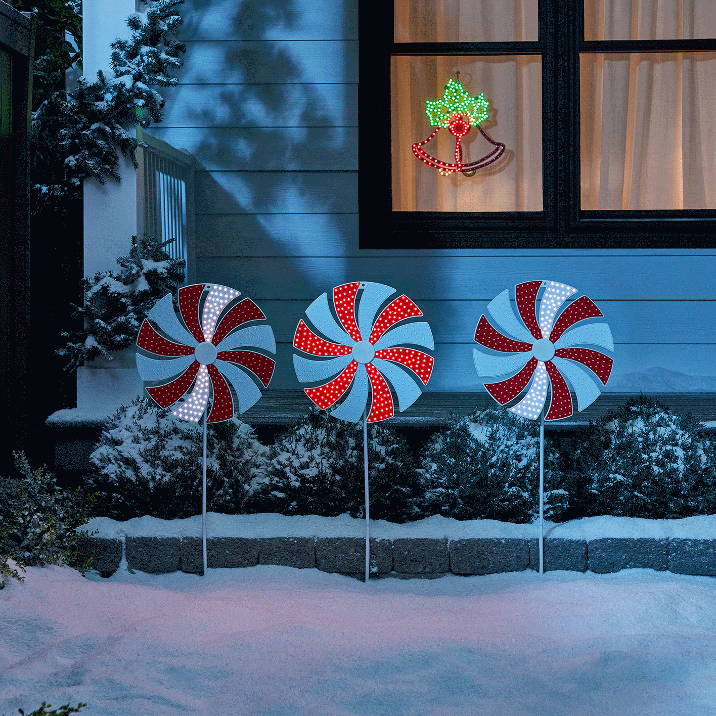 Trois piquets animés avec motif canne de bonbon ultra-brillants CANVAS dans une cour et une décoration de cloches des fêtes animées ultra-brillantes dans une fenêtre. 