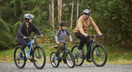 A woman, man, and young boy riding bikes on a trail in a wooded area.