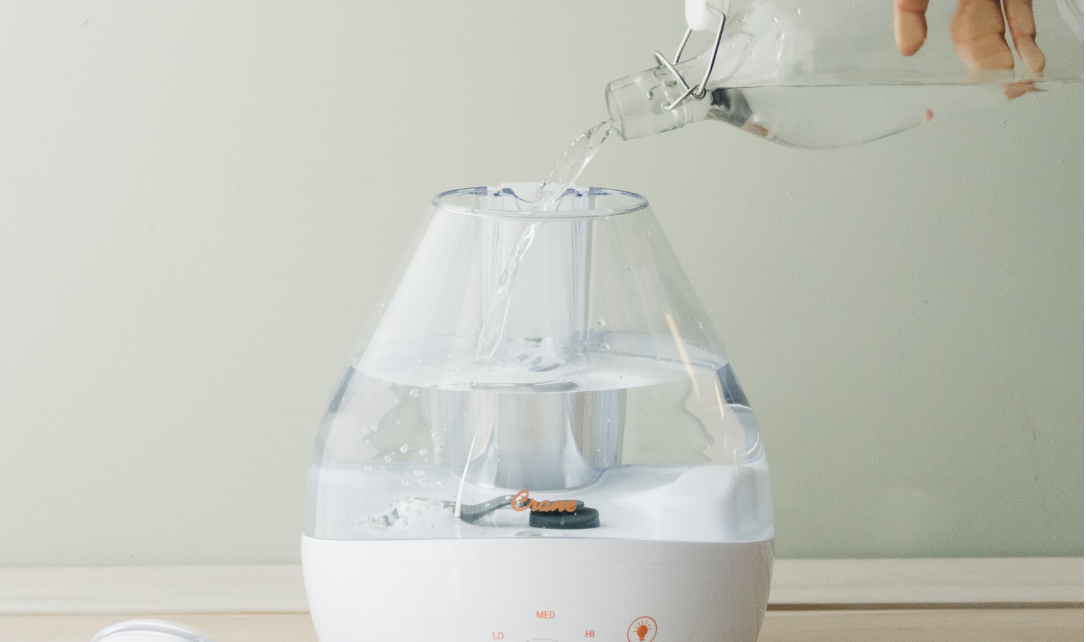 An adult pouring water from a bottle into a Crane Top Fill Ultrasonic humidifier.