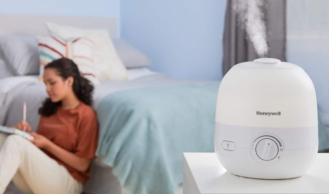 A Honeywell CLR Humidifier Diffuser in a bedroom with a woman sitting on a floor nearby.
